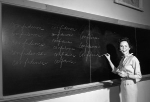 1950s Teacher In Front Of Classroom Writing Confidence On Blackboard